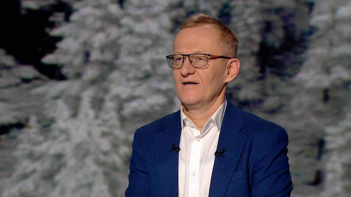 Portret mężczyzny w okularach i granatowej marynarce na tle zimowego krajobrazu.