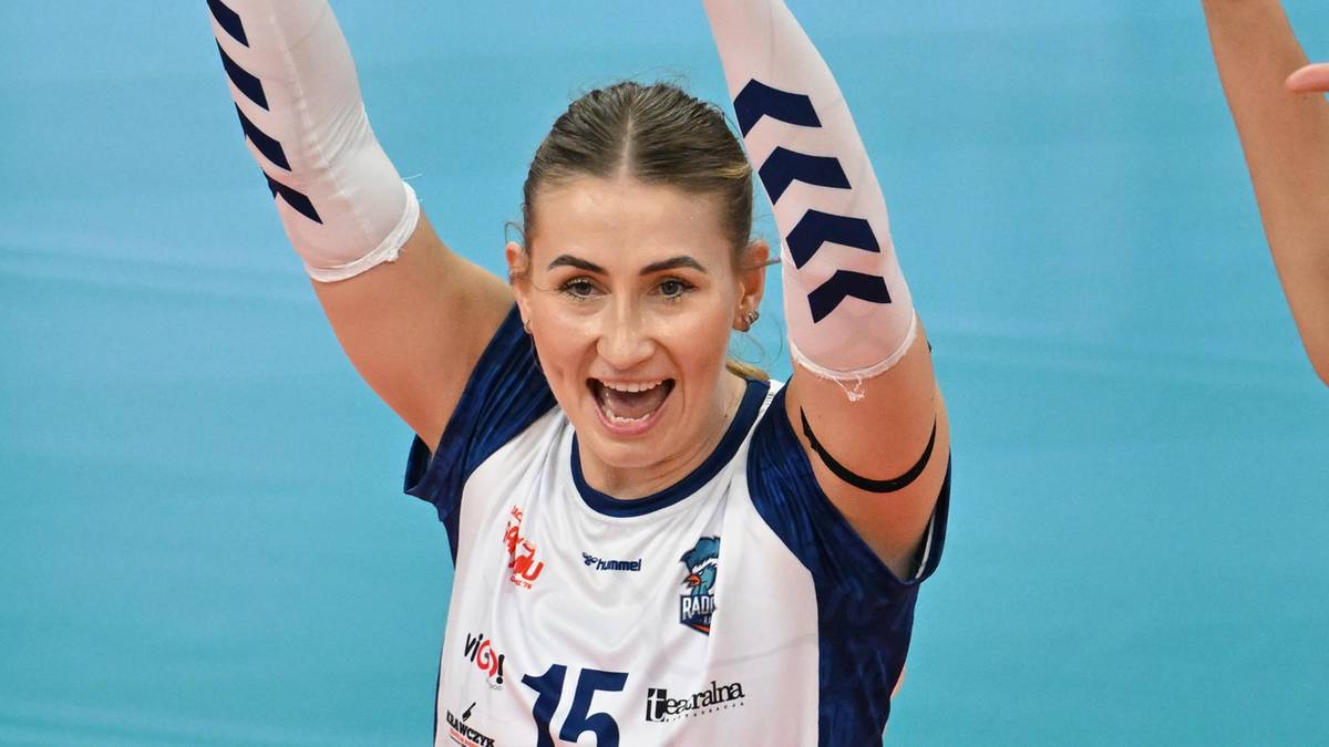 Siatkarki w białych koszulkach z niebieskimi elementami cieszą się ze zwycięstwa, podnosząc ręce do g&oacute;ry.