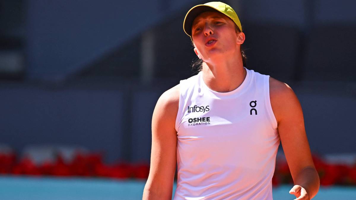 Tenisistka Iga Świątek w żółtej czapce i białej koszulce, patrząca w górę z zaciętą miną.