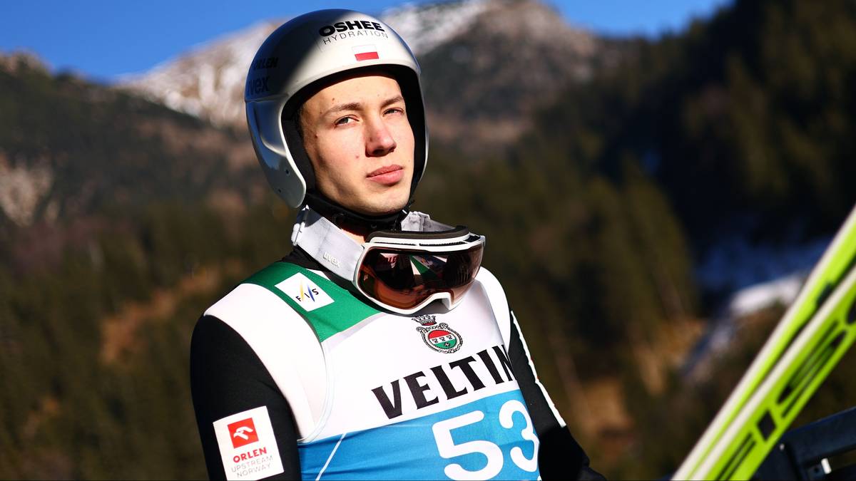 Skoczek narciarski w kasku i goglach na tle g&oacute;rskiego krajobrazu.