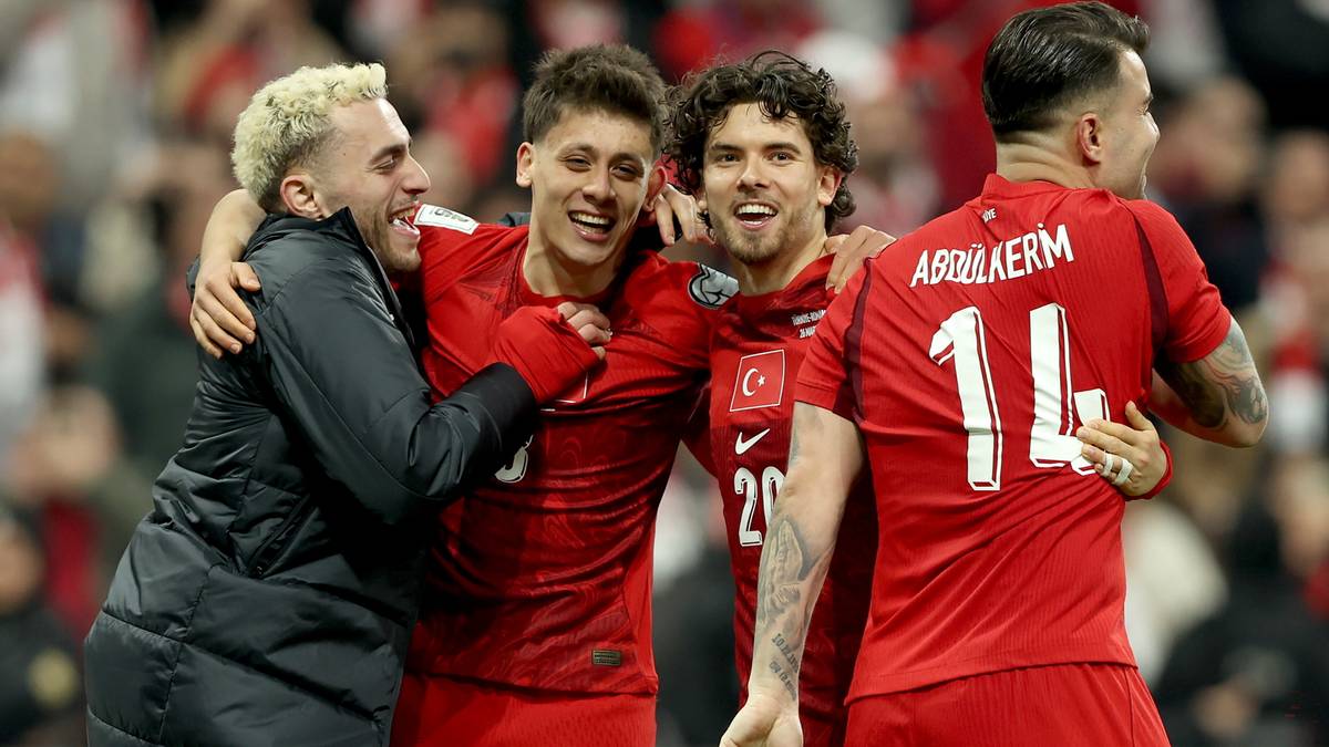Czterech piłkarzy reprezentacji Turcji w czerwonych strojach, obejmujących się i okazujących radość po zwycięskim meczu.