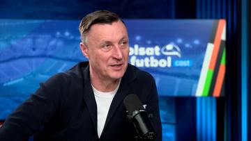 Tomasz Hajto, były polski piłkarz, wypowiada się przed mikrofonem na tle niebieskiego ekranu z logo "Polsat Futbol".