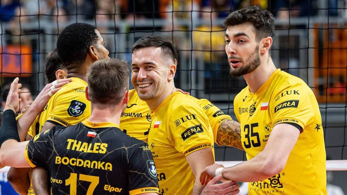 Siatkarze w ż&oacute;łtych koszulkach cieszący się ze zwycięstwa na boisku siatkarskim.