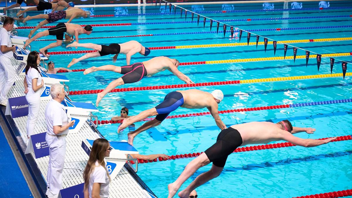 Zawodnicy pływacy startują w wyścigu z bloków startowych w basenie.