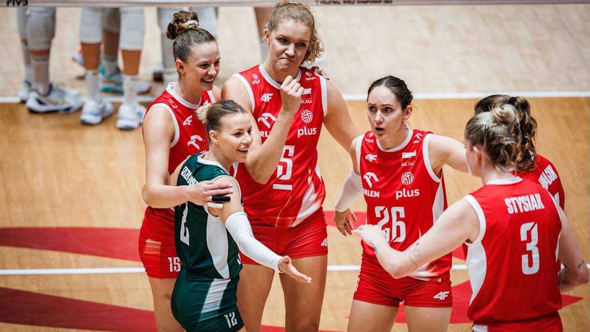 Grupa siatkarek w czerwonych strojach z biało-zielonym strojem w środku, radośnie celebrująca zwycięstwo na boisku siatkarskim.