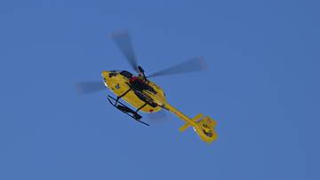 Ż&oacute;łty helikopter ratunkowy w locie na tle błękitnego nieba.