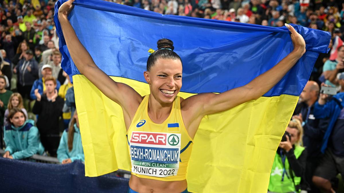 Uśmiechnięta lekkoatletka z Ukrainy, owinięta w ukraińską flagę, po zwycięstwie na zawodach "Monachium 2022".