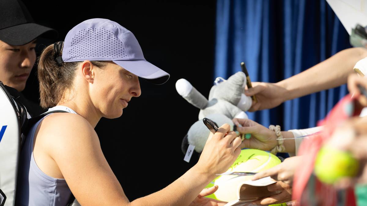 Tenisistka podpisuje autografy z pluszową zabawką w pobliżu.