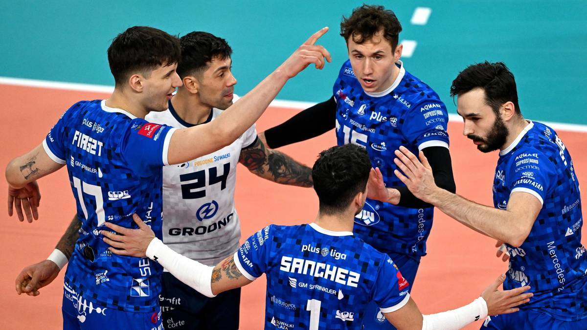 Pięciu siatkarzy w niebieskich strojach, skupionych wokół jednego z nich, który wskazuje palcem w górę.