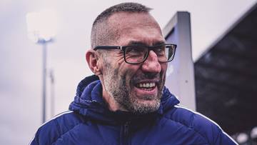 Marek Papszun, trener Rakowa Częstochowa, w okularach i kurtce sportowej, uśmiecha się.