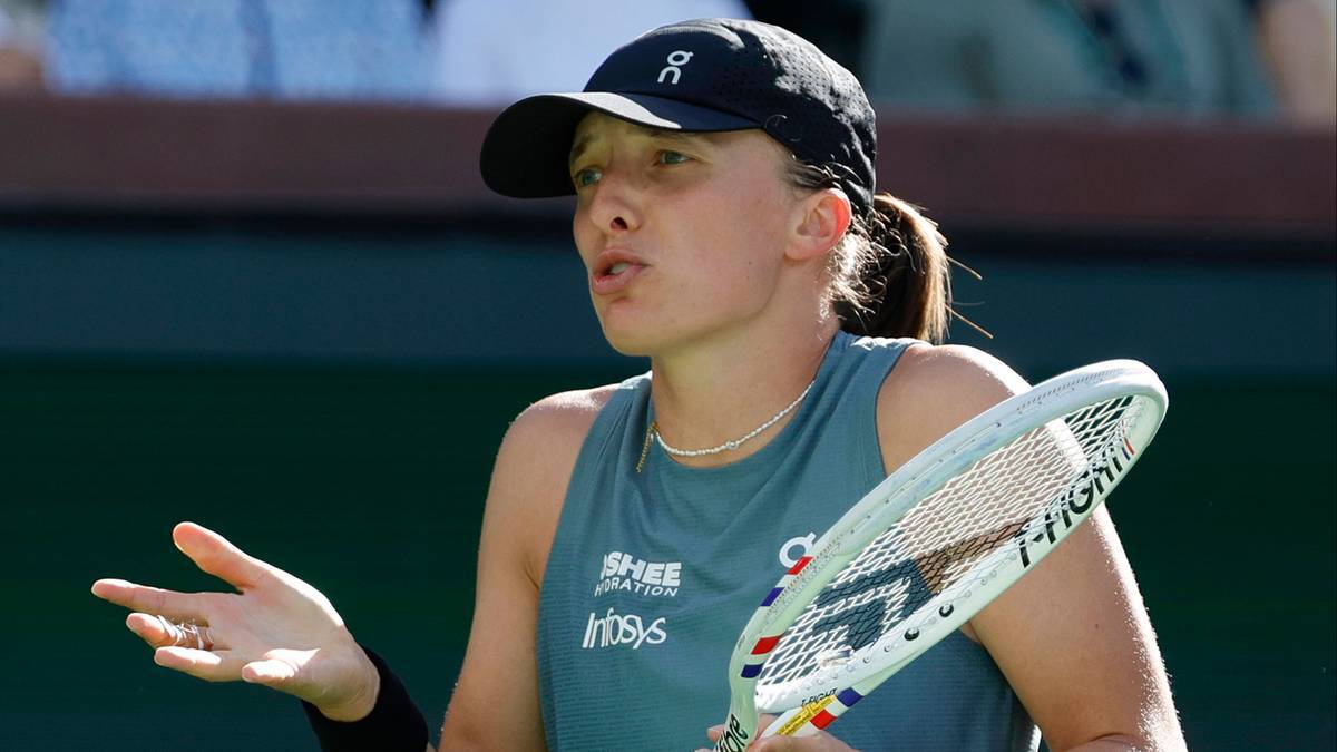 Tenisistka w czapce z daszkiem i sportowym topie trzyma rakietę tenisową i gestykuluje prawą ręką.