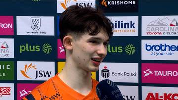 Maksymilian Granieczny, młody mężczyzna z ciemnymi włosami, uśmiecha się, trzymając mikrofon przed ustami. W tle znajduje się grafika telewizyjna z logotypami sponsor&oacute;w.