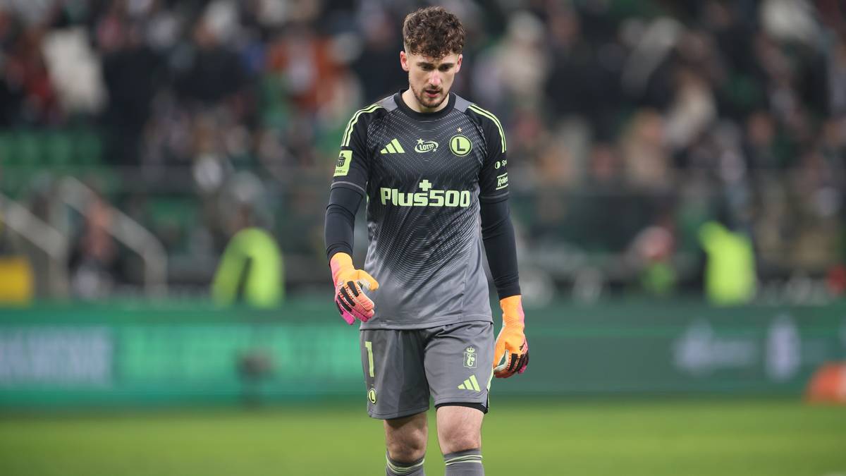 Młody bramkarz w szarej koszulce piłkarskiej z numerem 1 na plecach, stojący na boisku.