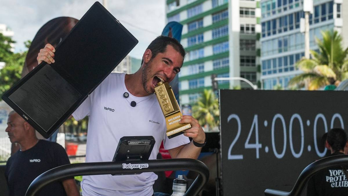 Mężczyzna trzymający trofeum i gryzący je, stojący na bieżni na świeżym powietrzu.