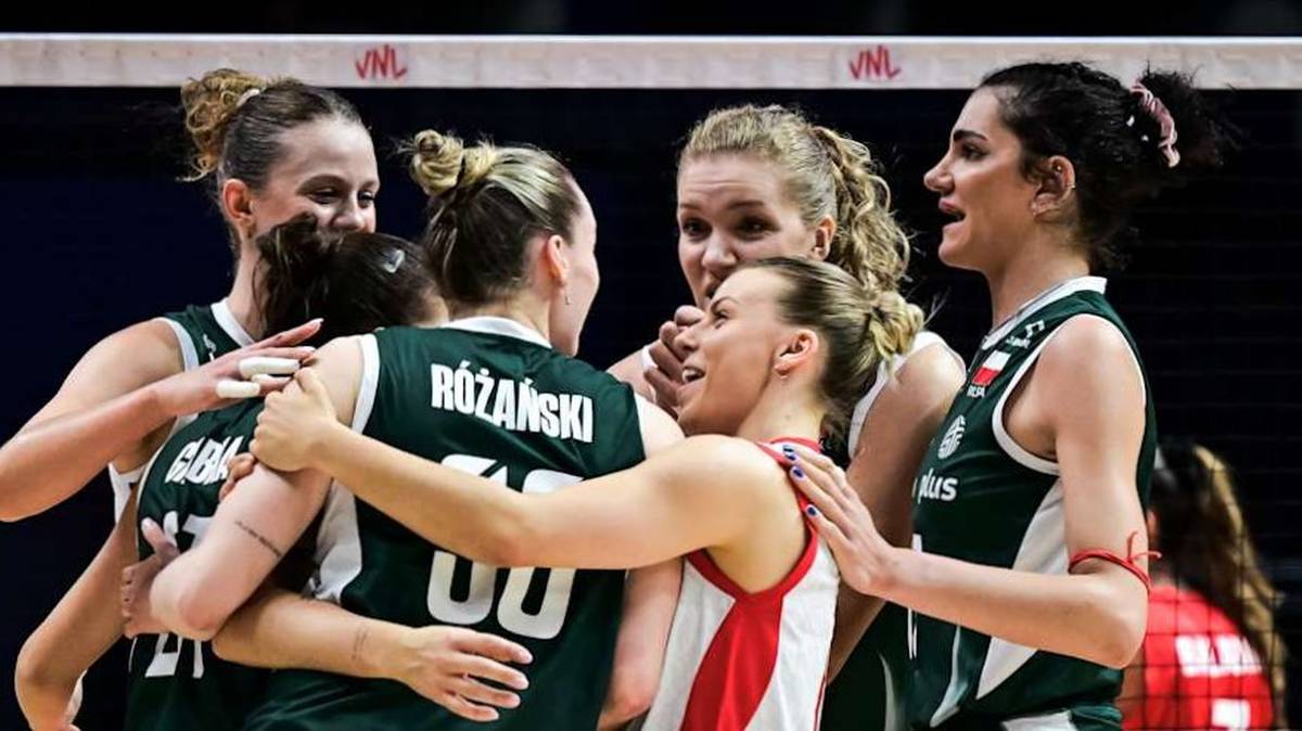 Siedem zawodniczek z drużyny siatkarskiej w zielonych koszulkach z białymi numerami i napisami, ściskają się radośnie w geście zwycięstwa na tle ciemnej sali gimnastycznej.