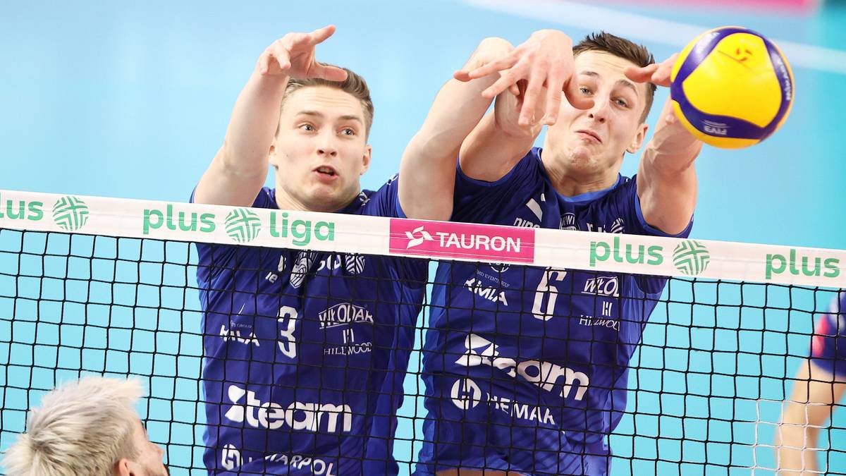Dw&oacute;ch siatkarzy w niebieskich strojach blokuje atak przeciwnika podczas meczu.