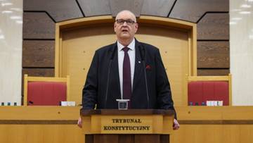 Mężczyzna w garniturze i krawacie stoi za m&oacute;wnicą z napisem "Trybunał Konstytucyjny".