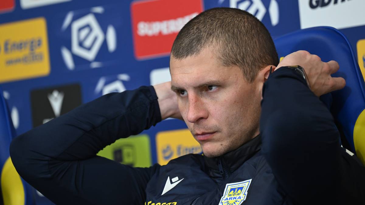 Mężczyzna w ciemnej kurtce sportowej zaciska ręce za głową, spoglądając w bok.