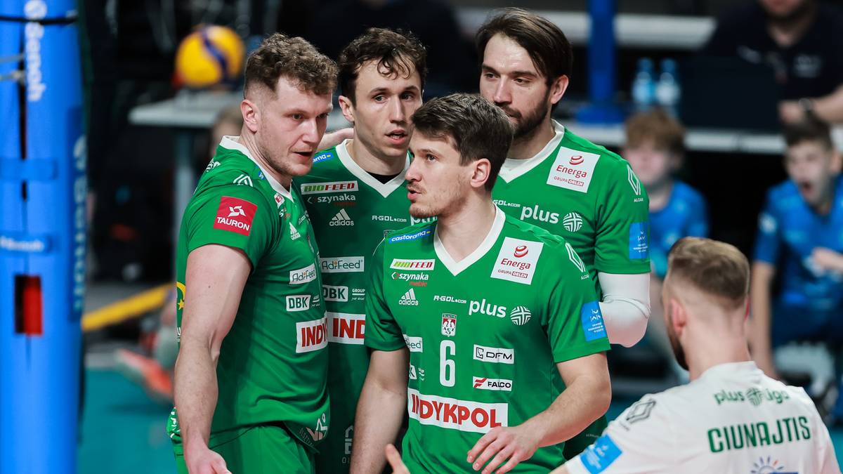 Grupa siatkarzy w zielonych strojach sportowych stoi na boisku, rozmawiając ze sobą.