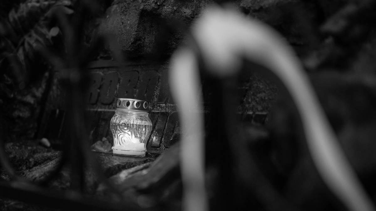 Szklane, płonące kadzidełko na kamiennej podstawie, otoczone przez ciemność i zamazane kontury roślin.