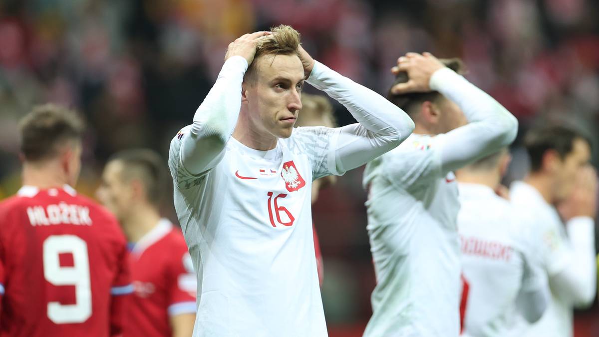 Piłkarz w białej koszulce reprezentacji Polski, z numerem 16, trzyma się za głowę w geście rozpaczy. Inni piłkarze w tle r&oacute;wnież wyglądają na przygnębionych.