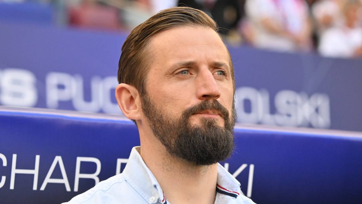 Mężczyzna z brodą w jasnej koszuli patrzy w bok.