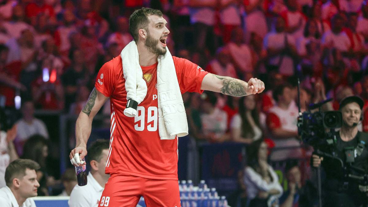 Siatkarz w czerwonej koszulce z numerem 99 i ręcznikiem na szyi, podczas emocjonującej akcji na boisku.