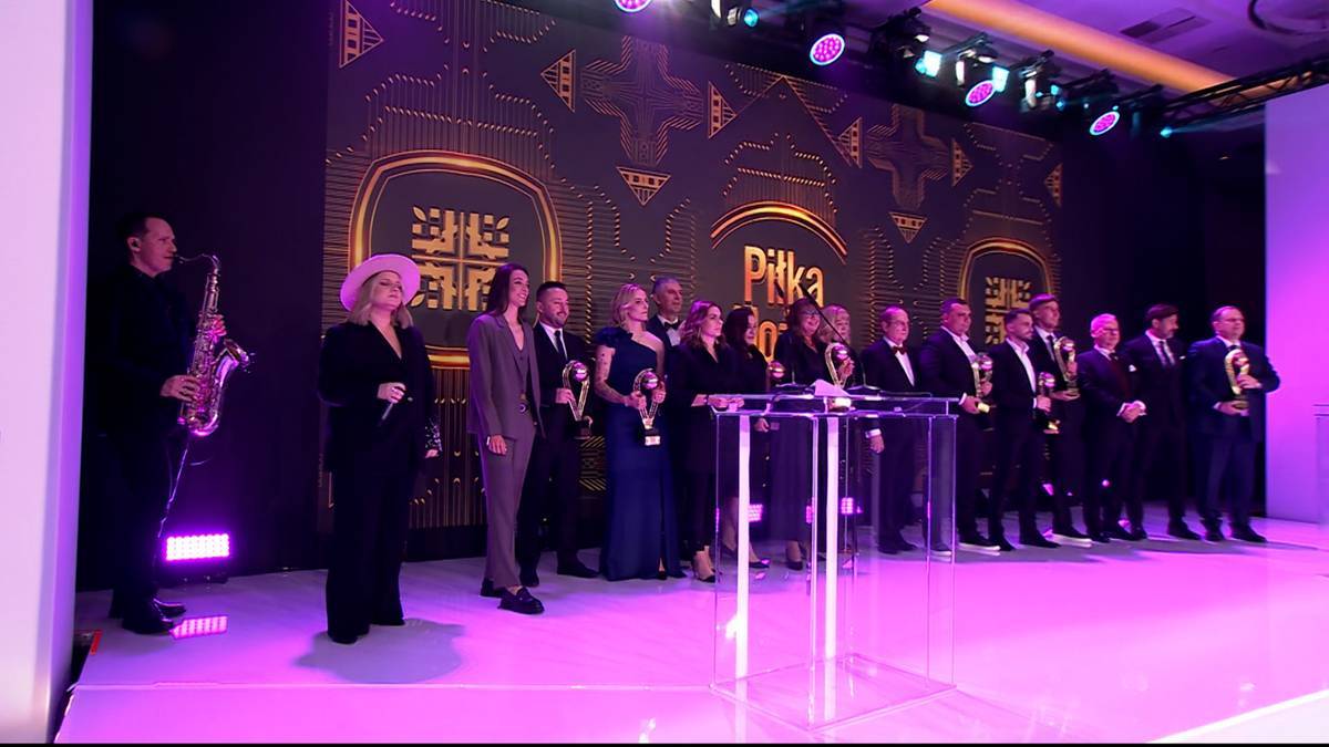 Grupa os&oacute;b stoi na scenie, niekt&oacute;rzy trzymają statuetki, za nimi widnieje podświetlone logo "Piłka Nożna".