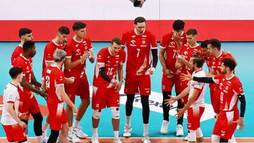 Grupa siatkarzy w czerwonych strojach sportowych z białymi elementami stoi w gru