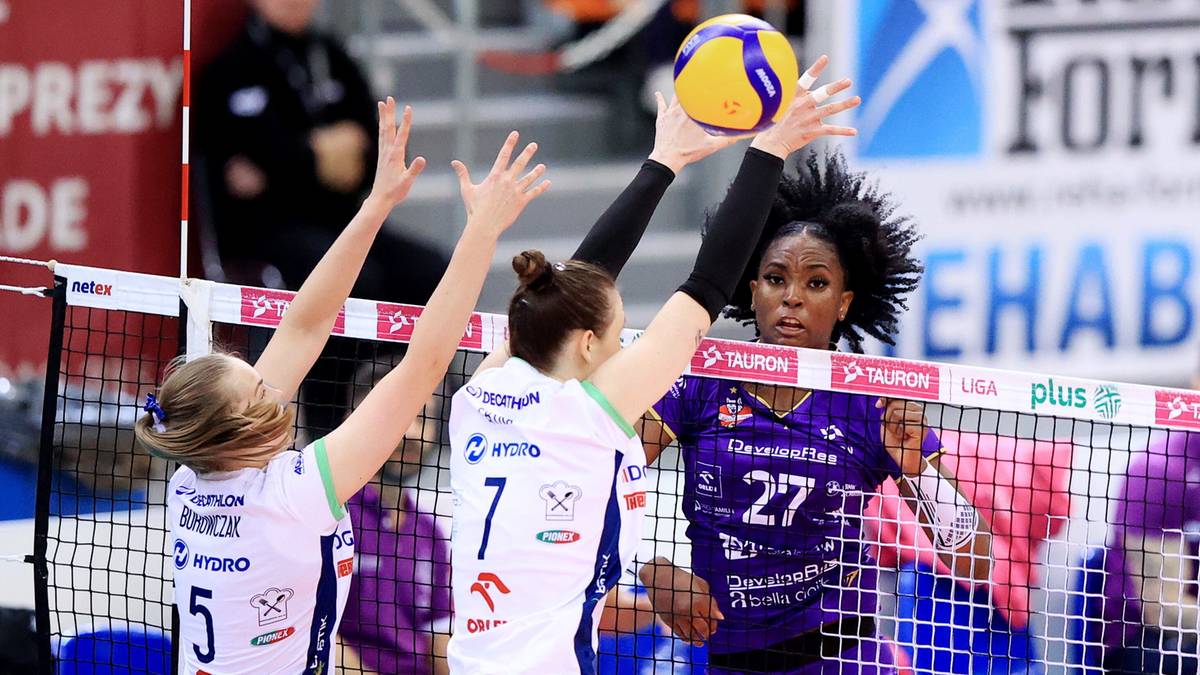Siatkarki blokują atak przeciwniczki podczas meczu.