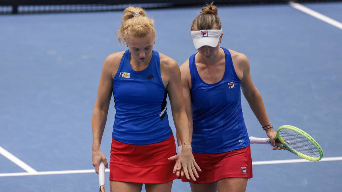 Dwie tenisistki w niebieskich koszulkach i czerwonych spódniczkach, idące obok siebie po korcie tenisowym.