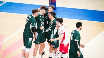 Grupa siatkarzy w zielonych strojach sportowych dyskutuje na boisku, jeden z nich ma biało-czerwony strój.