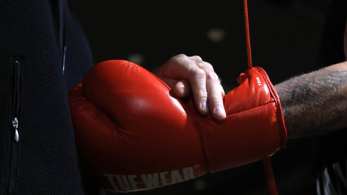 Dłoń osoby wkładana jest do czerwonej rękawicy bokserskiej.