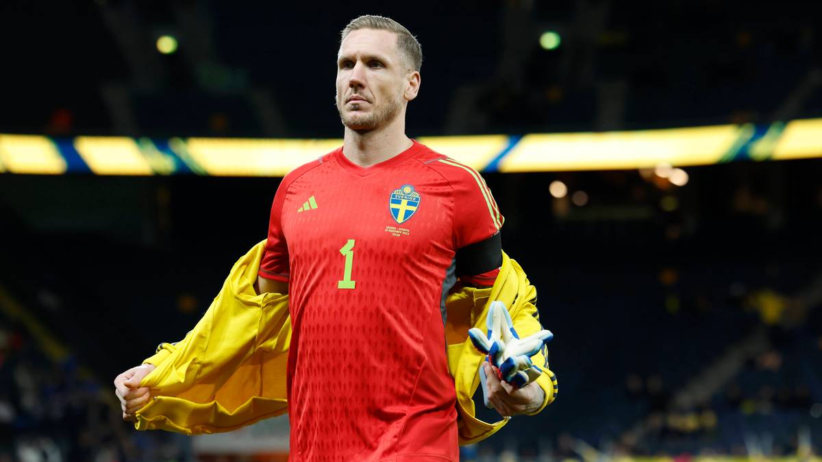 Bramkarz reprezentacji Szwecji w czerwonej koszulce z numerem 1, zdejmujący ż&oacute;łtą kurtkę.