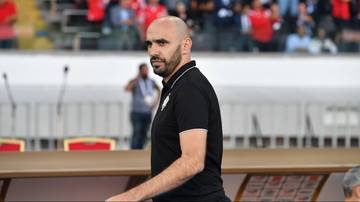 Walid Regragui, trener reprezentacji Maroka, w czarnej koszulce polo na tle trybun stadionu.