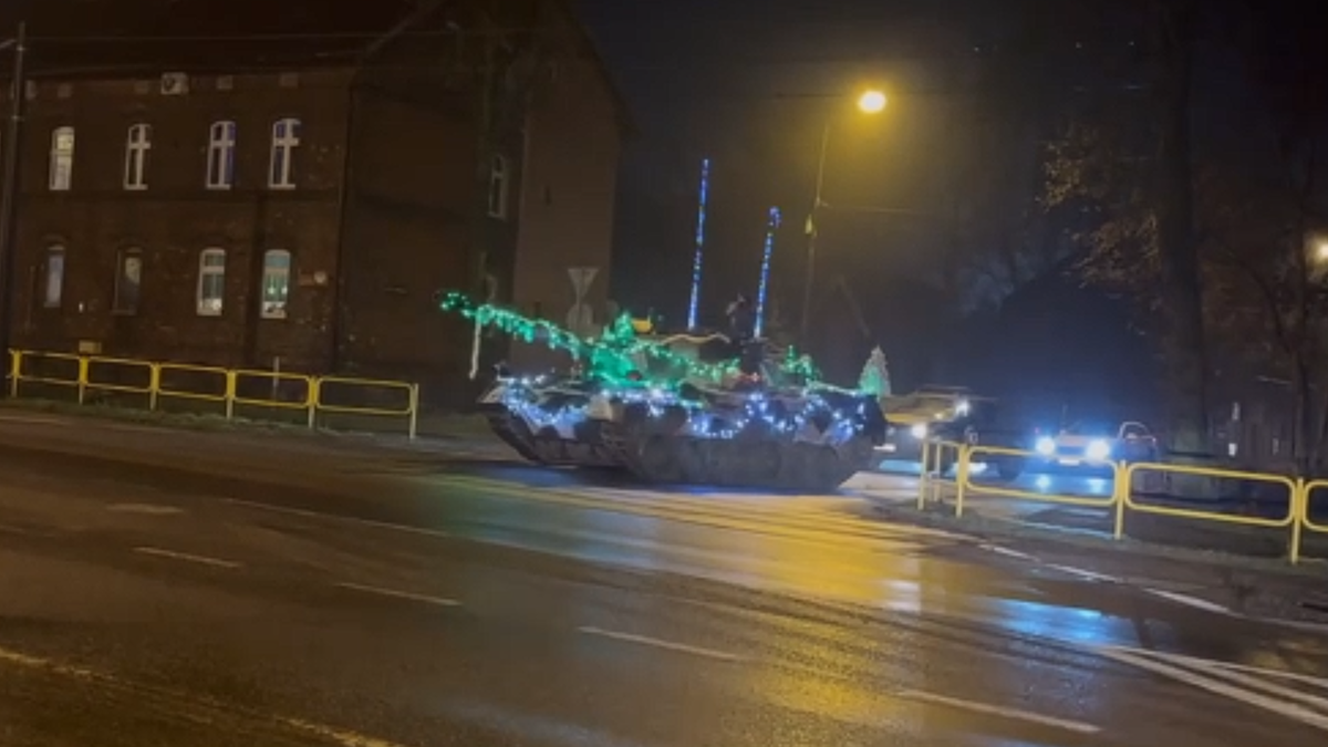 Czołg Leopard I ozdobiony świątecznymi lampkami i łańcuchami jedzie nocą po ulicy.