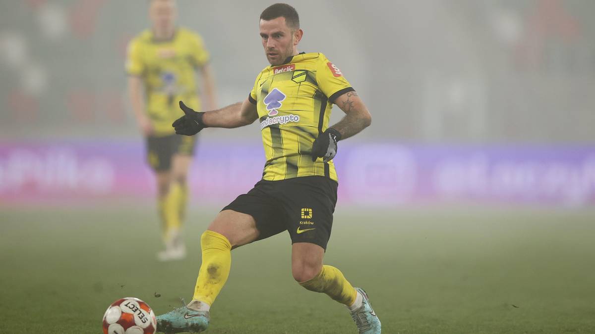 Piłkarz w ż&oacute;łto-czarnej koszulce prowadzi piłkę na boisku.