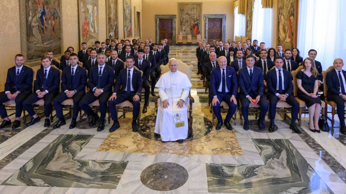 Papież Leon XIV siedzi na krześle pośrodku dużej grupy piłkarzy i działaczy Interu Mediolan, wszyscy ubrani w eleganckie stroje.